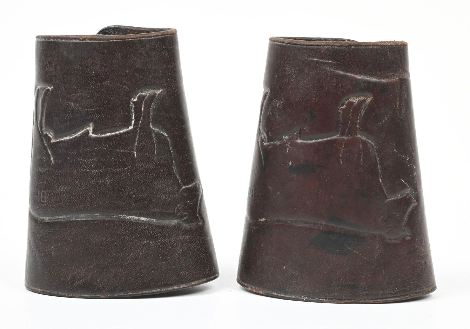 LEATHER CUFFS TOOLED WITH BULL DESIGN: Western cowboy cuffs with bull motif by Heiser of Denver. Maker stamped brass buttons. Each, 5" long by 3 1/4" diameter. CONDITION: Good with one cuff button present but separated from the snap portio