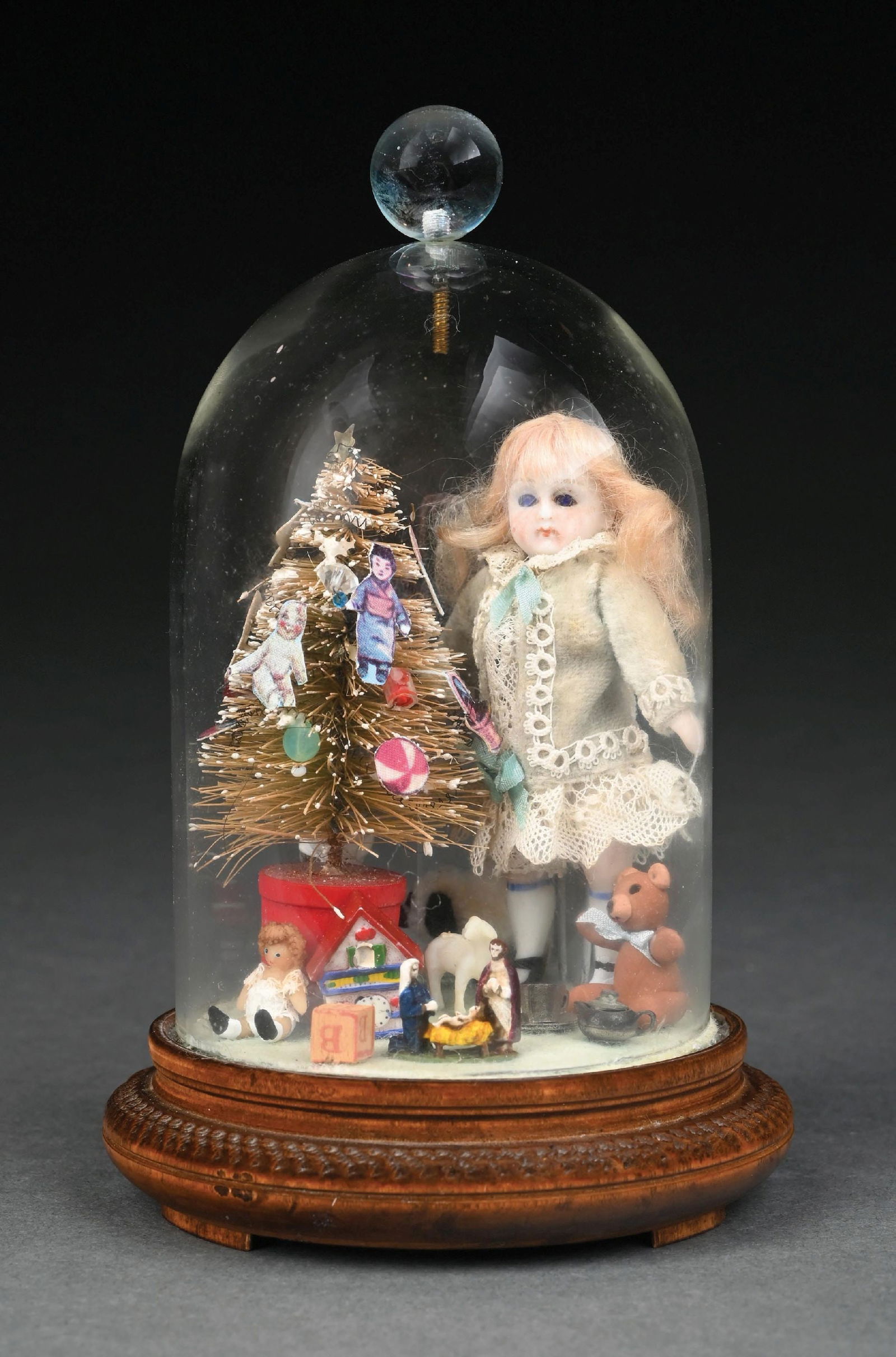 SMALL BISQUE DOLL ENCLOSED IN GLASS NEXT TO SMALL CHRISTMAS TREE: Figures and presents around tree. Doll looks like it has original clothing and displays well. Condition: (Very Good - Excellent). Dimensions: 6" T.