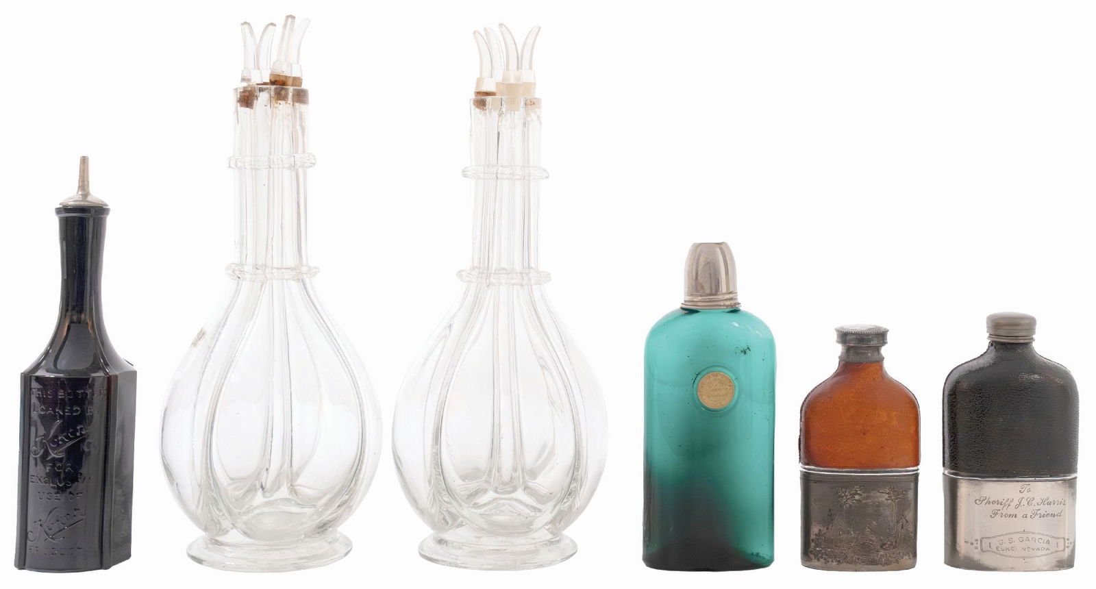 COLLECTION OF 6 FLASKS AND CLEAR GLASSWARE: A collection of three pocket flasks and three pour bottles. (A) Two barber bottles that reads "Loaned by Koken Barber Supply Co.". (B) Bottle with four separate sections in the interior of the bottle
