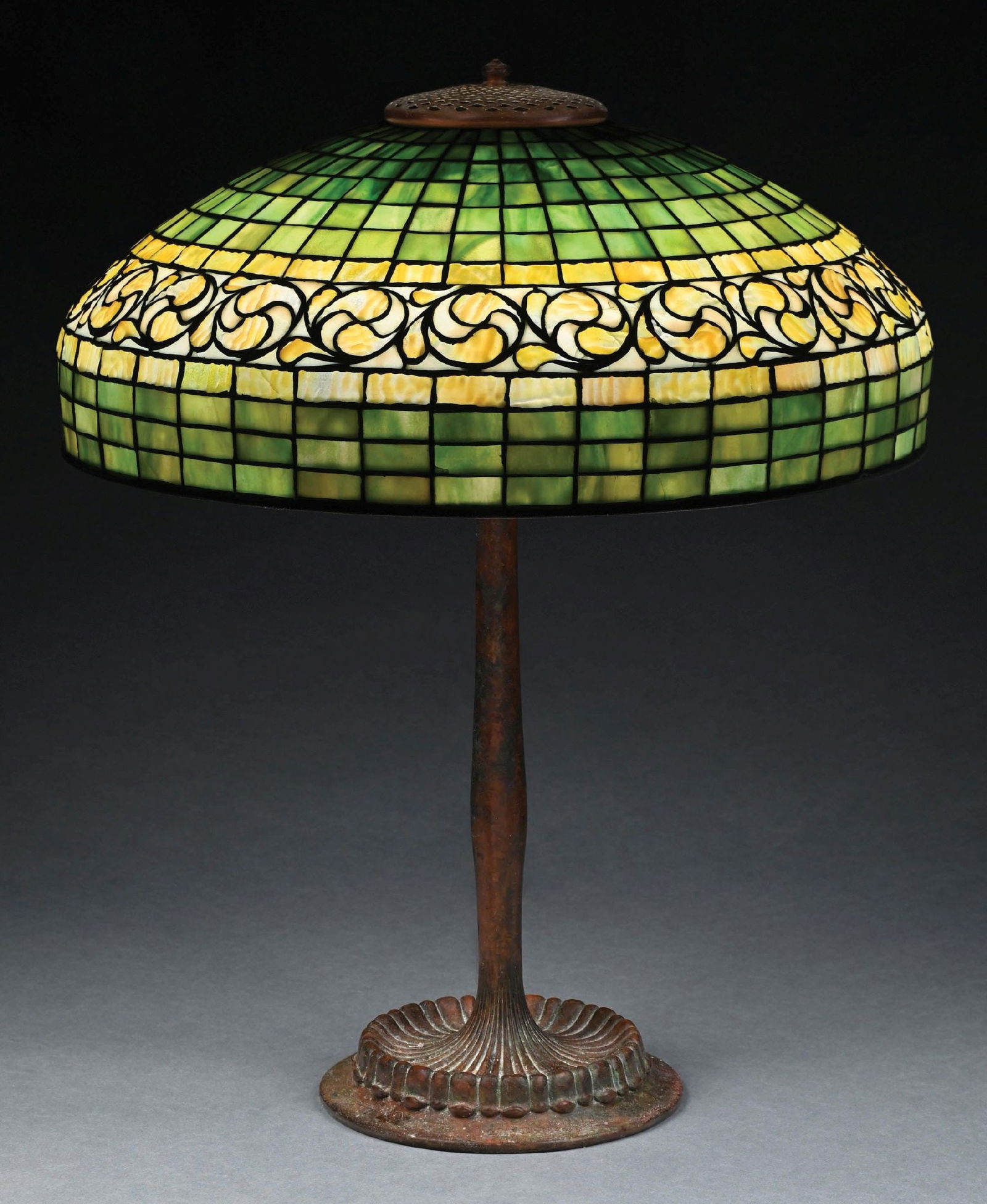 TIFFANY STUDIOS SWIRLING LEMON LEAF LEADED GLASS TABLE LAMP: A lovely leaded glass table lamp by Tiffany Studios. The 18" diameter shade features a geometric background of multicolored green tiles, with a very artistic progression of darker green at the apertur
