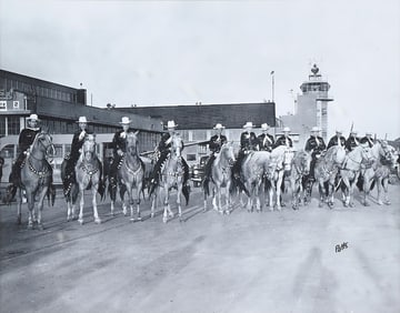 BLACK AND WHITE PHOTO OF A PROCESSION OF HORSES AND RIDERS