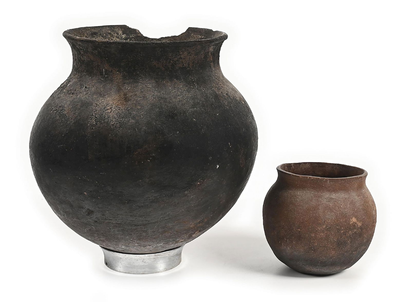 LOT OF 2: POTTERY PREHISTORIC OLLAS: (A) A large plainware olla with incrustation around rim and on the interior. Pieces missing from rim. With stand - 13" Dia. x 14 1/2" T. (B) Pottery olla with blackened base formed from micaceous clay