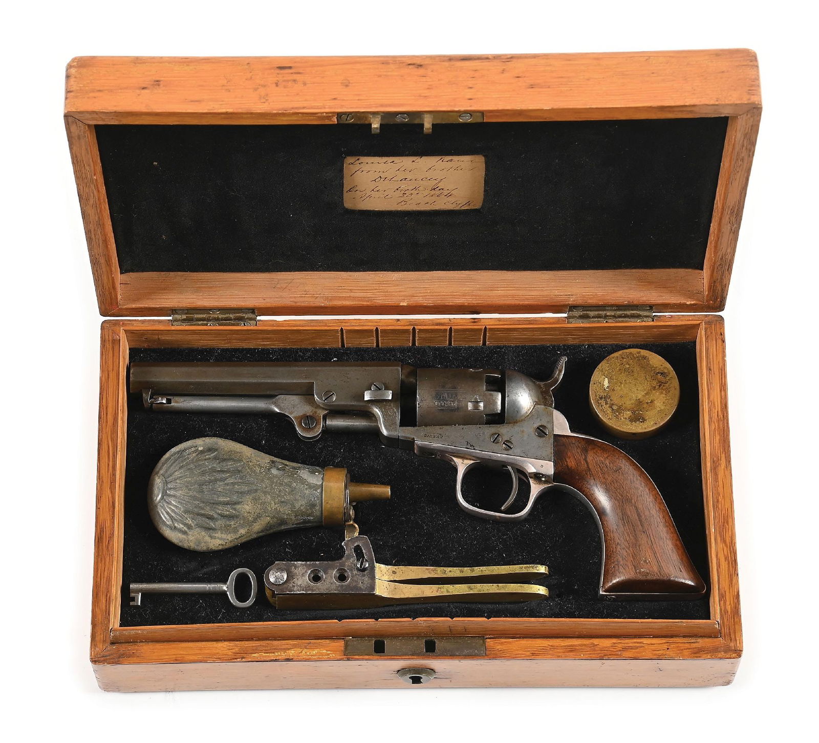 (A) CASED COLT MODEL 1849 POCKET PERCUSSION REVOLVER: Dates to 1860. Standard octagon barrel with two-line New York address. All matching numbers including wedge and lever. Features plated straps, one-piece walnut grips, and 80% stage coach cylinder scen