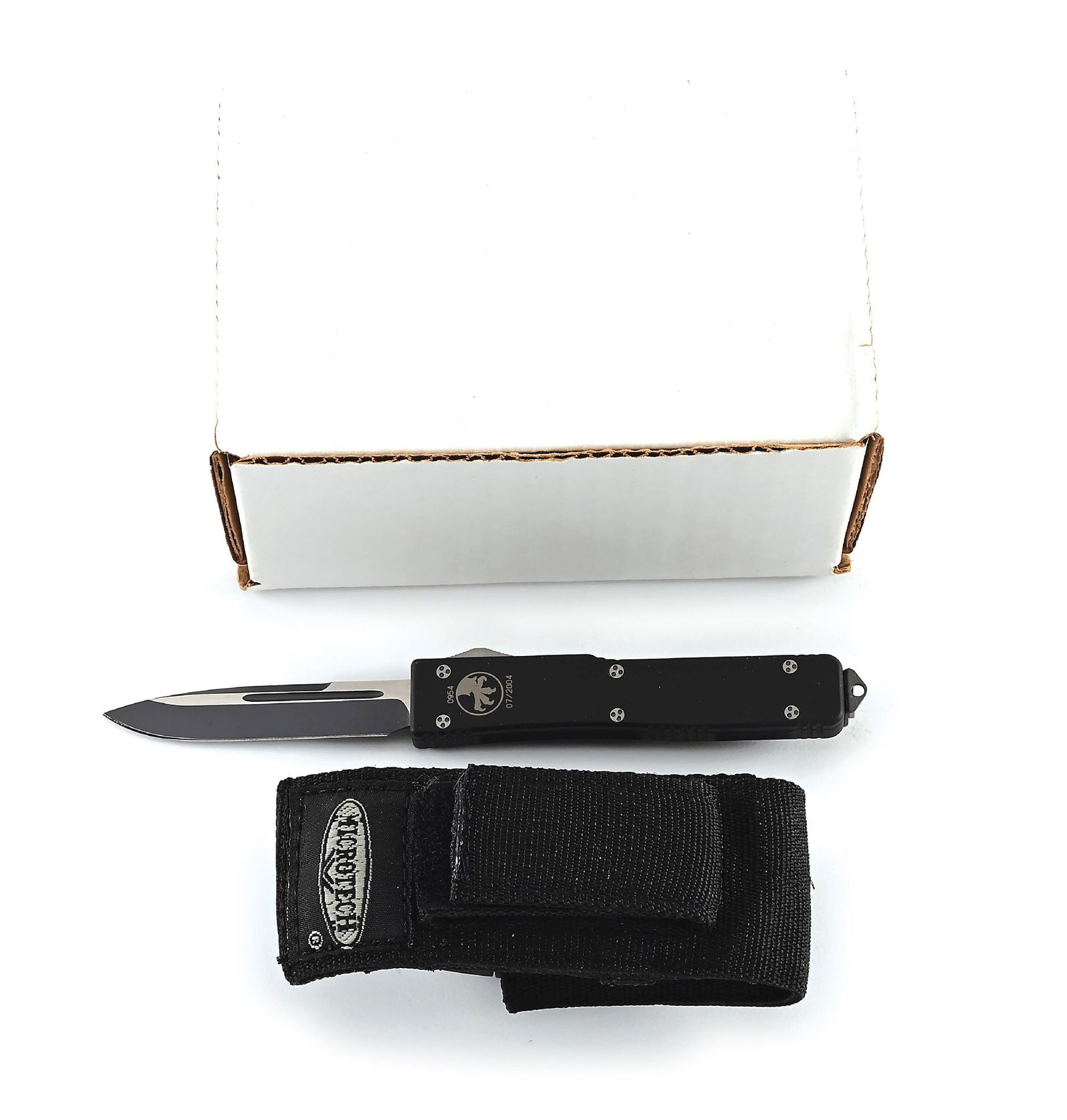 BOXED MICROTECH UTX-70 OTF AUTOMATIC KNIFE.: Microtech UTX-70 that features a two-tone black plain blade with swedge and fullers. Black aluminum frame numbered "0954" with Microtech eagle claw logo and dated "07/2004". Ramped thumbslide with