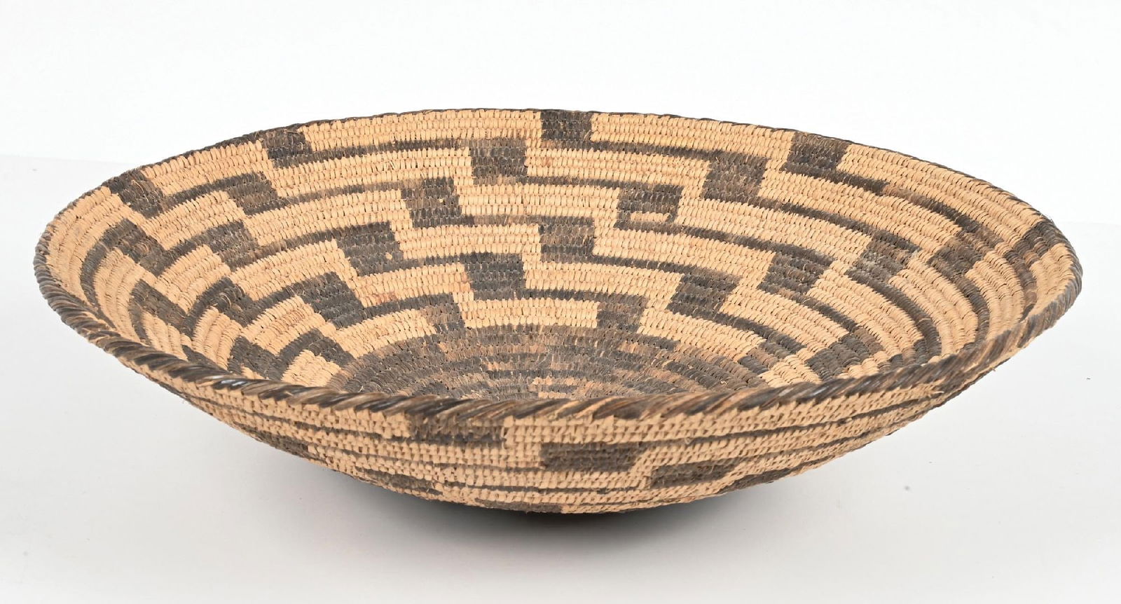 PIMA (AKIMEL O'ODHAM) BASKET: A flaring bowl with stepped radiating lines extending from a large circular design covering the base and the rim done with whipped stitching. Condition: With very few stitches missing. Dimensions: 15