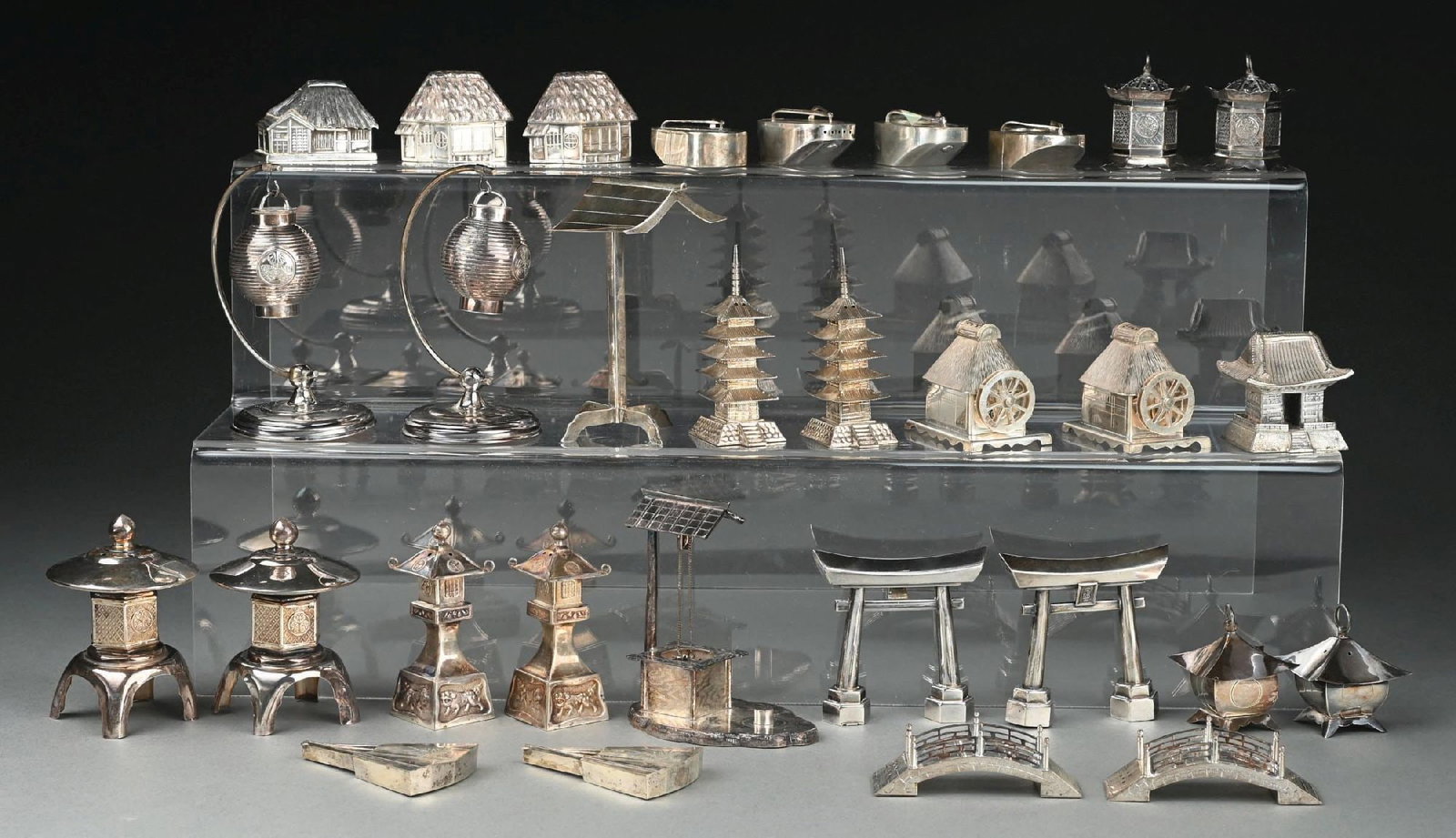 A GROUP OF JAPANESE STERLING FIGURAL SALTS AND PEPPER CASTERS: Including four in the form of huts with thatched roofs, a pair of lanterns, a pair of hanging censers, a pair of entrance gates, a pair of pagodas, a pair of sandals, and others. (30) Height of talles