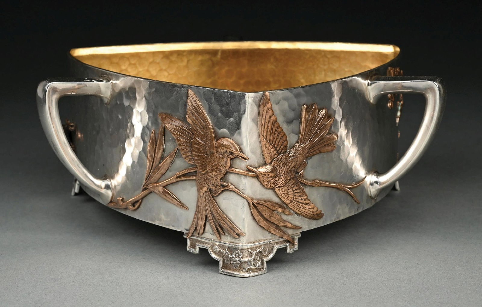 A GORHAM AESTHETIC PERIOD JARDINIERE: 19th Century. Triangular with curved sides applied with copper plants and two birds all on a hammer finish, then center of each side with a handle. Model number M1645. Extreme length: 9-1/2". Weight: 