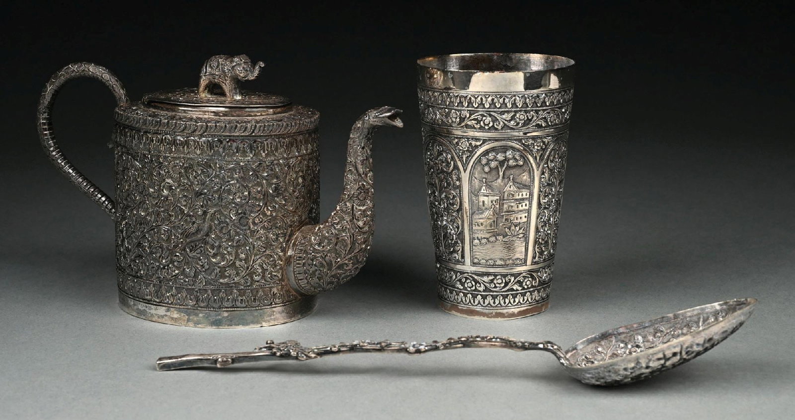 A SOUTH ASIAN SILVER TEAPOT: Of oval form with a elephant handle, the body chased allover with scrolling foliage and birds, unmarked; together with a beaker with similar decoration, with tapering sides, marked 925; and a Chinese 
