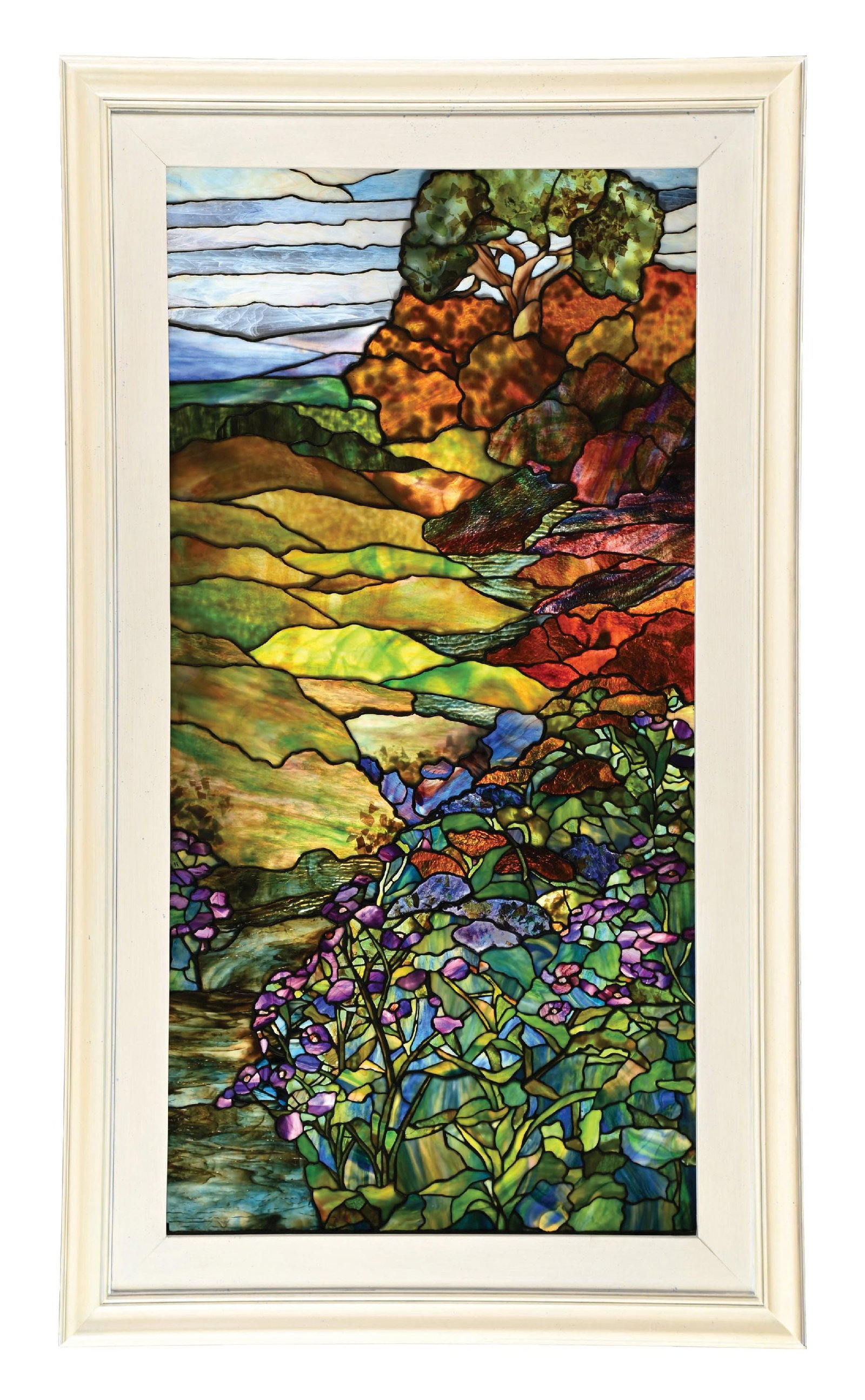 TIFFANY STUDIOS LANDSCAPE WINDOW W/ IRISES FROM THE SEYMOUR & EVELYN HOLTZMAN COLLECTION: An absolutely gorgeous example of a floral landscape stained glass window by Tiffany Studios. The window depicts a scenic landscape with rolling hills, trees, and a blue sky in the background, with