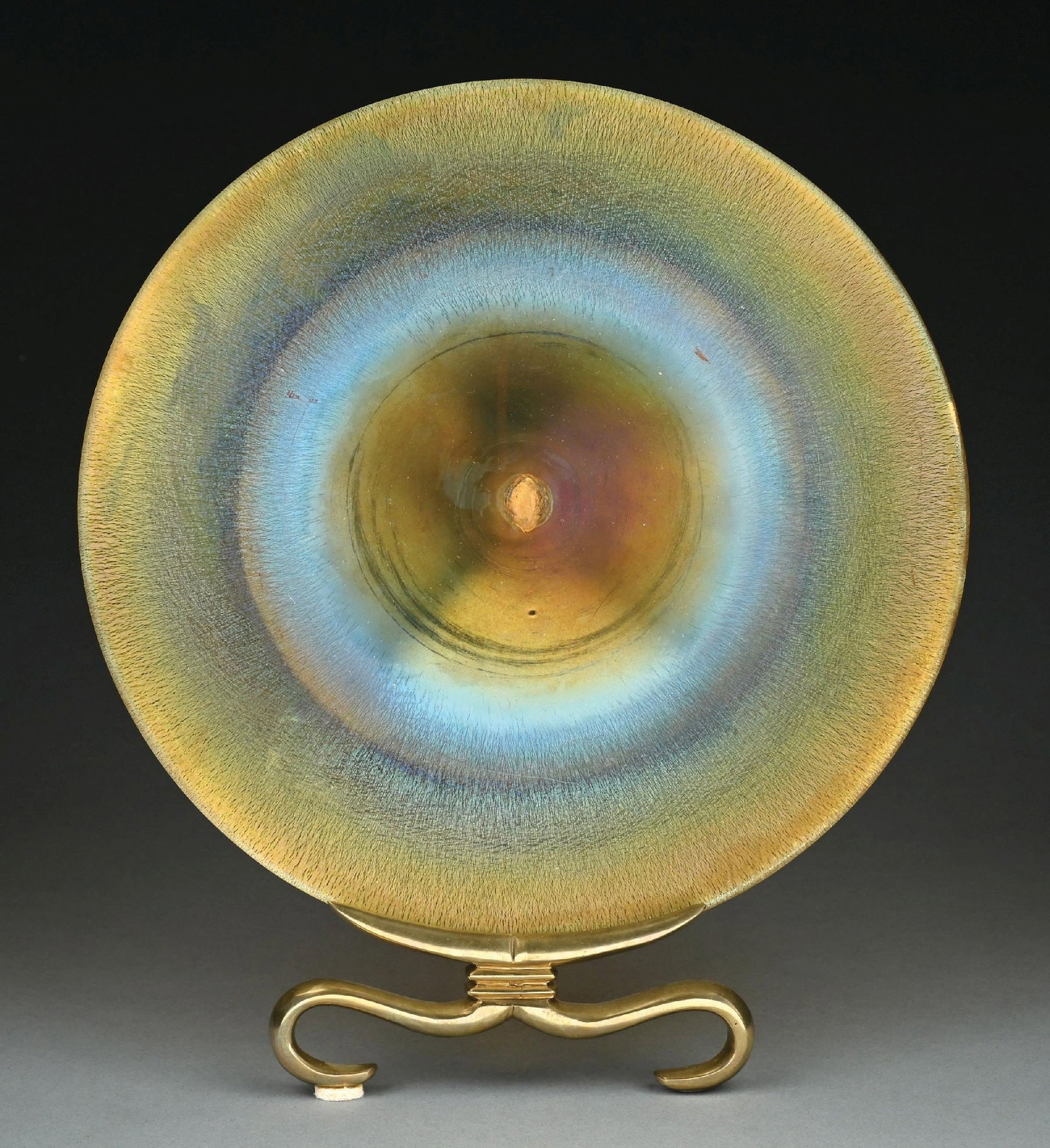 LARGE TIFFANY STUDIOS FAVRILE GLASS CHARGER WITH BRONZE STAND: A beautiful and rare early Tiffany Studios favrile glass charger from the Seymour and Evelyn Holtzman Collection. The 14-1/2" favrile glass charger is composed of beautifully iridescent gold favrile