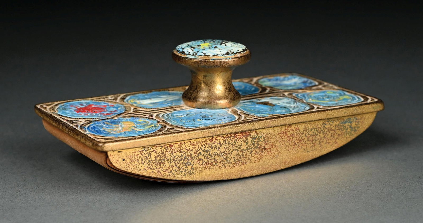 TIFFANY STUDIOS BRONZED & ENAMELED ZODIAC ROCKER BLOTTER: A beautiful rocker blotter by Tiffany Studios. The bronze blotter is finished in acid-etched gold dore with blue enameled zodiac patterns decorating the top. The side of the blotter is signed "Tiffany