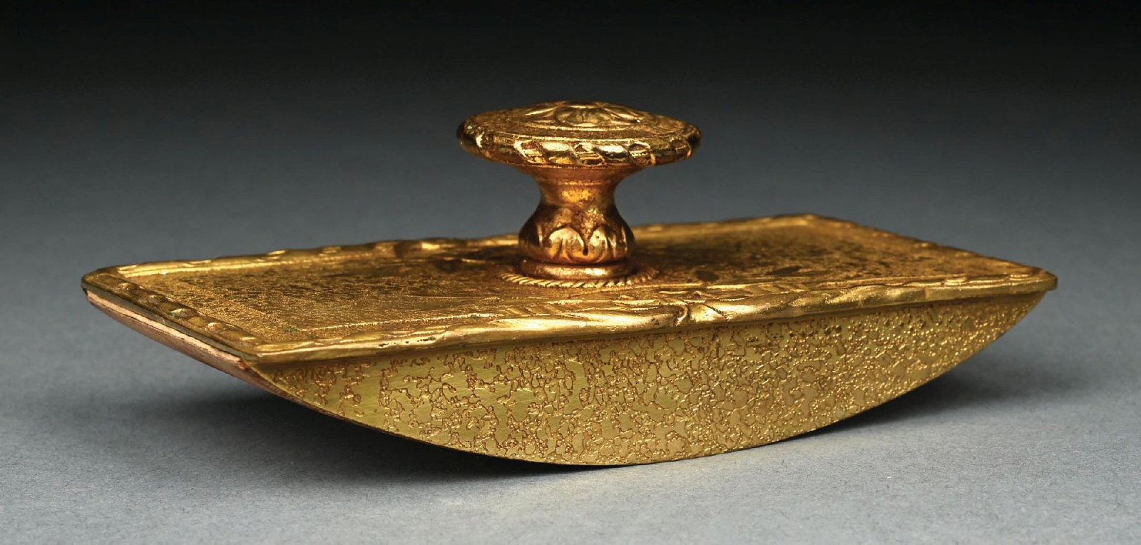 TIFFANY STUDIOS GOLD ROCKER BLOTTER: A lovely rocker blotter by Tiffany Studios. The rocker blotter is finished in an acid-etched gold dore with ribbon motif. Stamped to the side "Tiffany Studios New York 182". Condition: (Excellent).