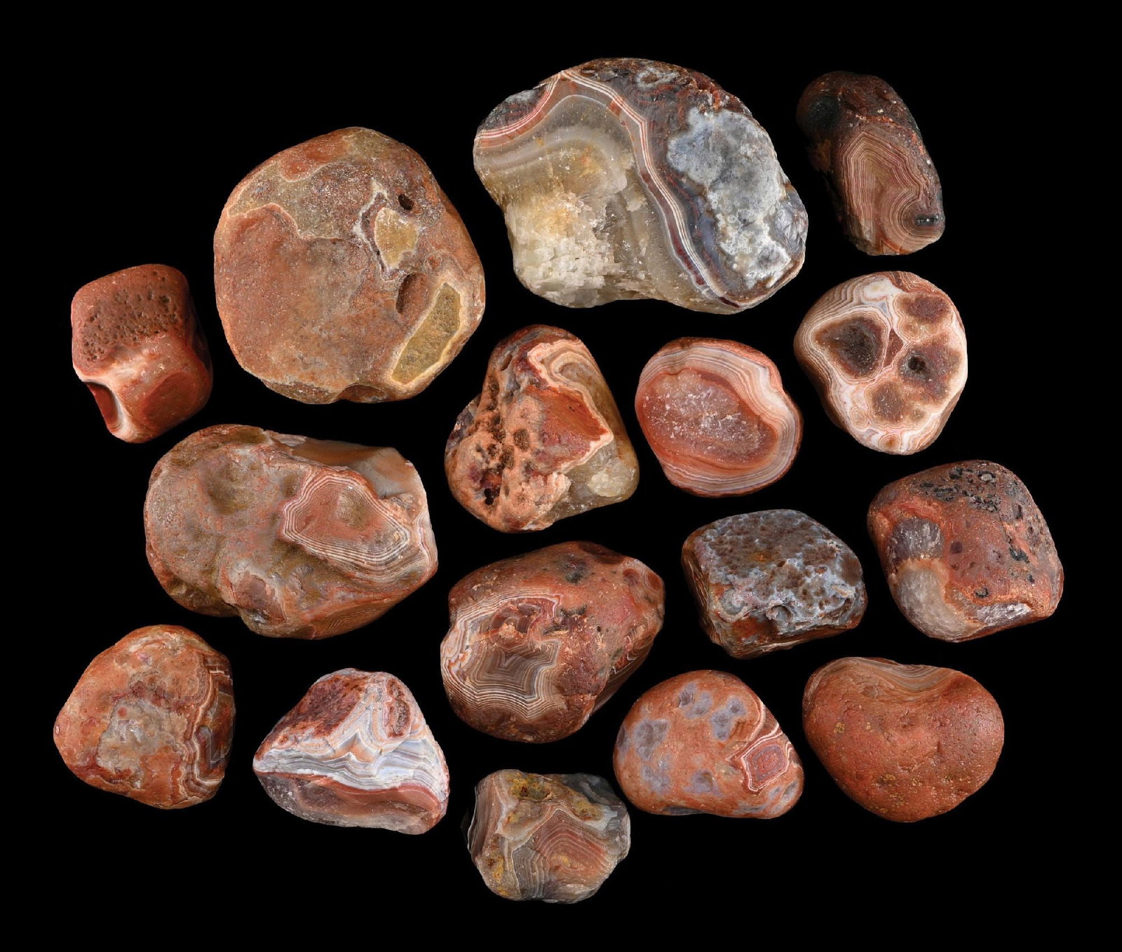 LARGE COLLECTION OF 16: RED AGATES: A collection of sixteen banded agate nodules formed in volcanic rock cavities. These banded chalcedony quartz specimens display red and brown coloration from iron and mineral impurities, with concentr