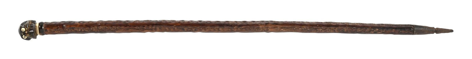 KNOTTED DRESS CANE: C. 1800s. A striking tiger’s eye skull-handled dress cane, featuring bone-inlaid eyes and a carved collar. The shaft is crafted from knotted wood and terminates in a metal spike ferrule.