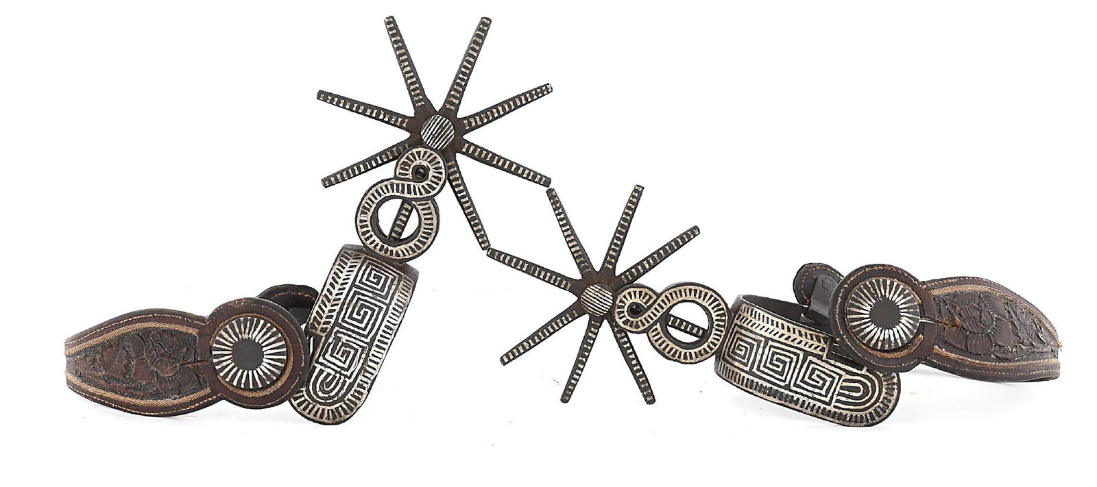 LARGE MEXICAN SPURS: Early 1900s Mexican charro style spurs. Inlaid on outside band with Greek key patterns and inside bears the silver initials "JU". They retain their original hand carved floral straps with traditional 