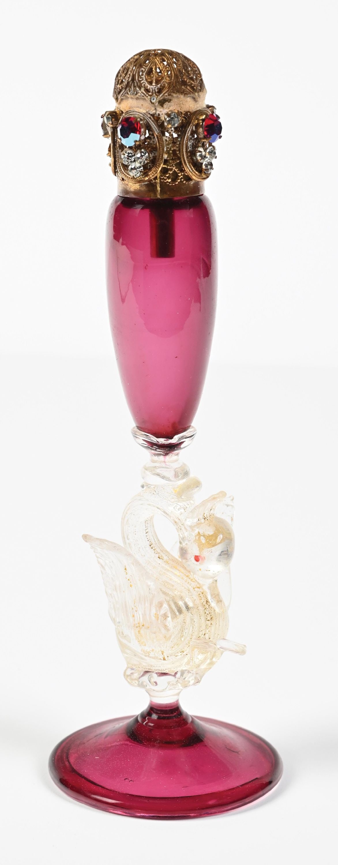 RUBY RED GLASS PERFUME BOTTLE WITH SWAM STEM: C. 1960s. A gorgeous DeVilbiss perfume with a ruby-red glass body with a clear swan stem infused with gold accents. The top of the pump perfume is in fantastic condition, adorned with functional metal