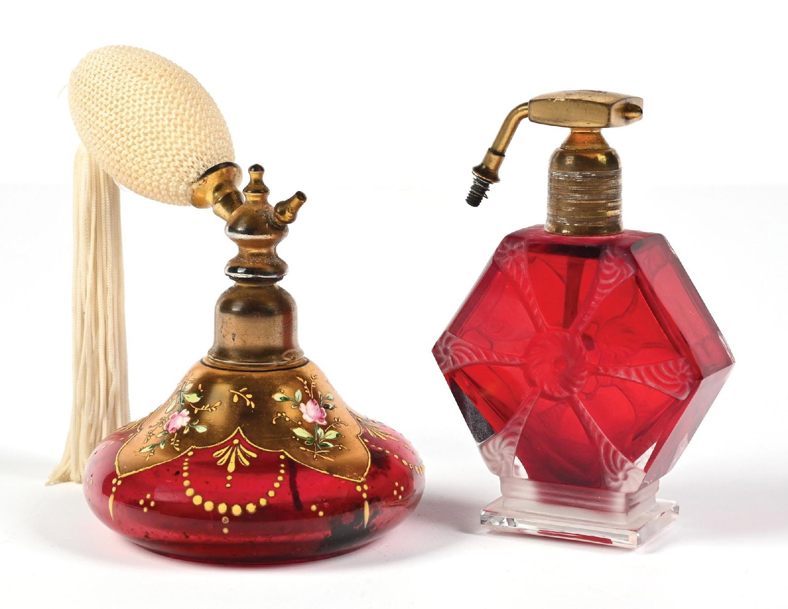 LOT OF 2: CRANBERRY GLASS PERFUME ATOMIZERS: C. 1900s. (A) A beautiful bohemian cranberry atomizer perfume with a rounded ornate glass body and intricate gold painted floral and beaded pattern with atomizer and cream tasseled puff. (B) A spectac