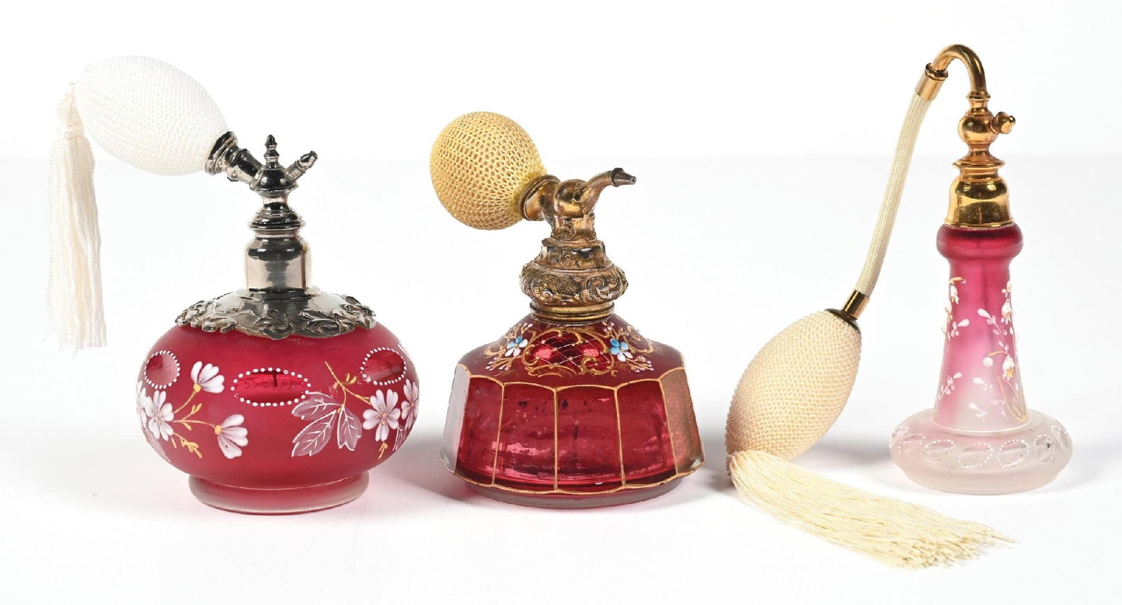 LOT OF 3: CRANBERRY GLASS PERFUMES WITH ATOMIZERS: C. 1800s. (A) A lovely cranberry glass perfume atomizer bottle featuring a silver-tone top and white floral enamel decorations. The rounded glass body has a frosted finish and features a functional wh