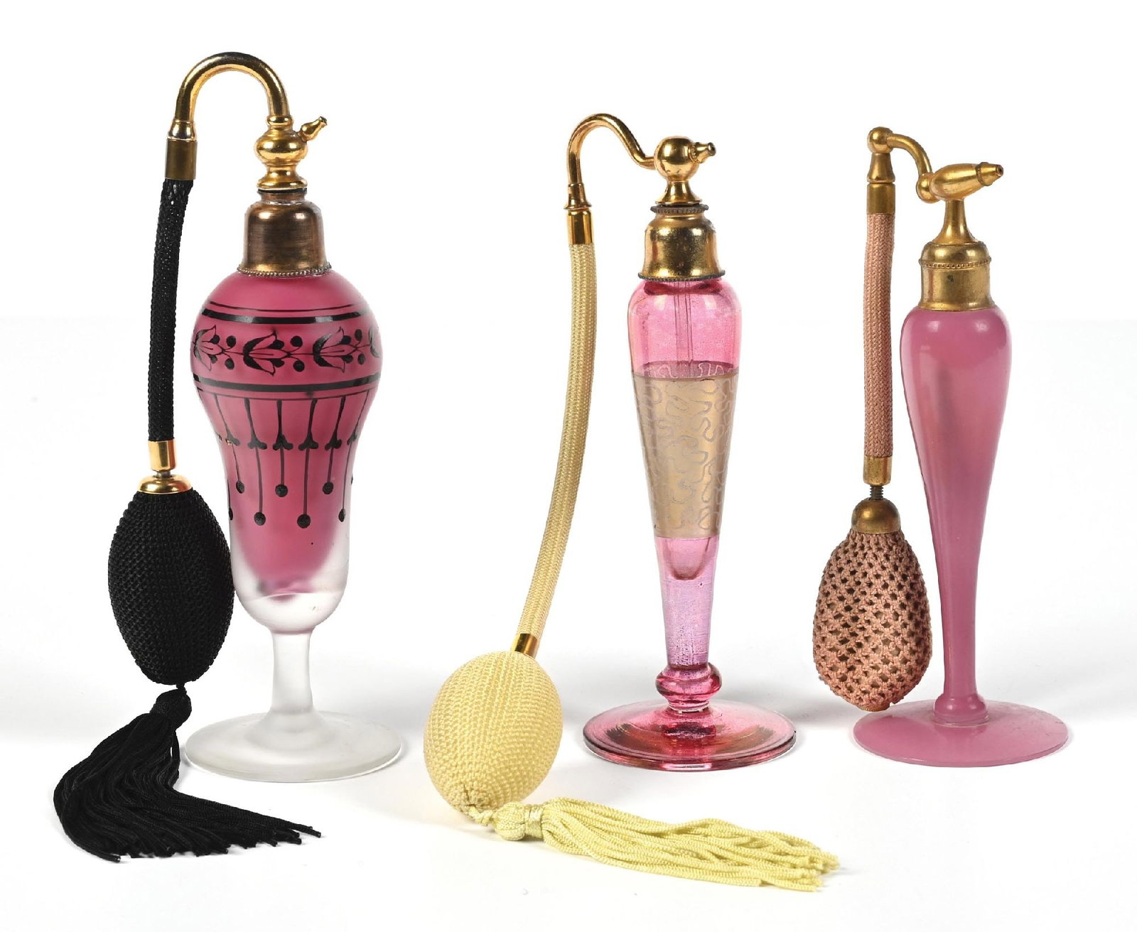 LOT OF 3: CRANBERRY PERFUMES WITH ATOMIZERS: C. 1920s-1930s. (A) A unique pink frosted perfume atomizer with a black enamel stylized floral pattern, gold-toned hardware and includes a black hose and a functional tasseled puff. (B) A lovely Art D
