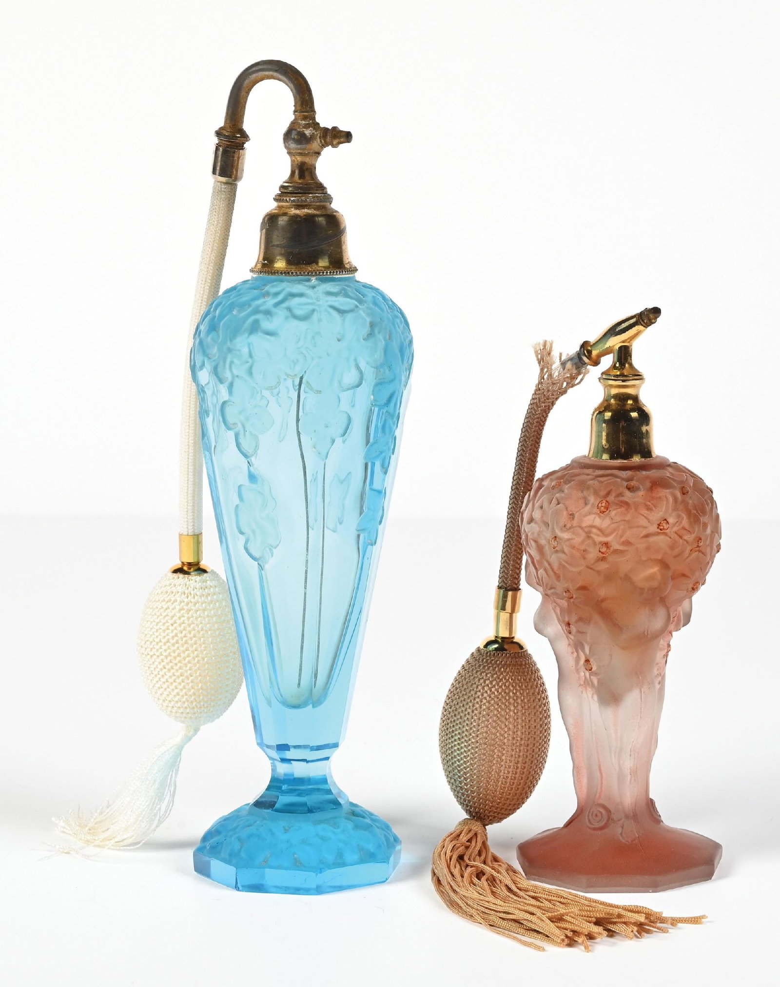 LOT OF 2: JOSEF SCHMIDT OPALESCENT BLUE & PINK PERFUME WITH FLORAL FIGURAL DESIGN: C. 1900s. (A) A lovely Josef Schmidt blue glass perfume atomizer. The bottle features a floral opalescent pattern, a brass-plated top, and an attached white mesh atomizer puff with tassels. (B) An