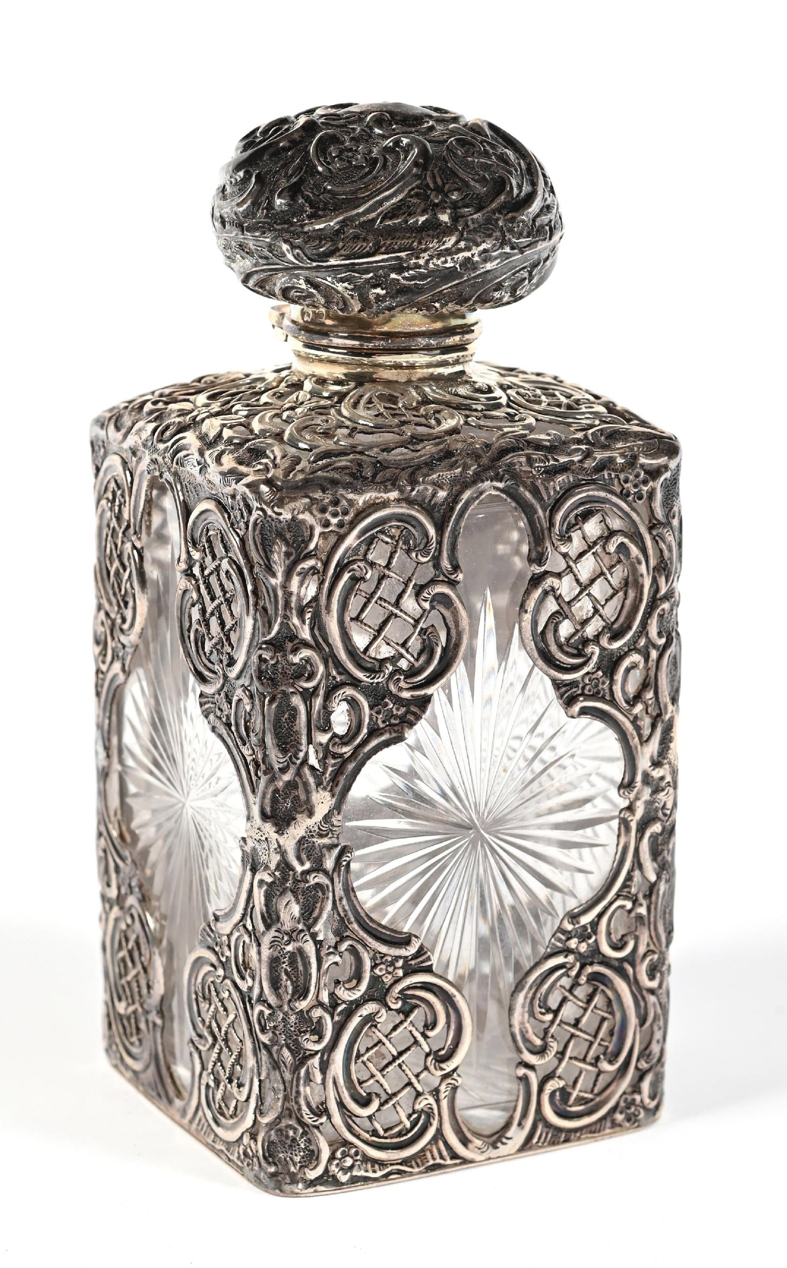 WILLIAM COMYNS CUT GLASS PERFUME WITH ORNATE SILVER CASING: C. 1893. A lovely William Comyns English crystal star-cut bottle with a silver casing. The elaborate silver overlay and hinged lid feature a dark patina. In great condition. 2 - 3/4" x 2 - 3/4" x 5 - 
