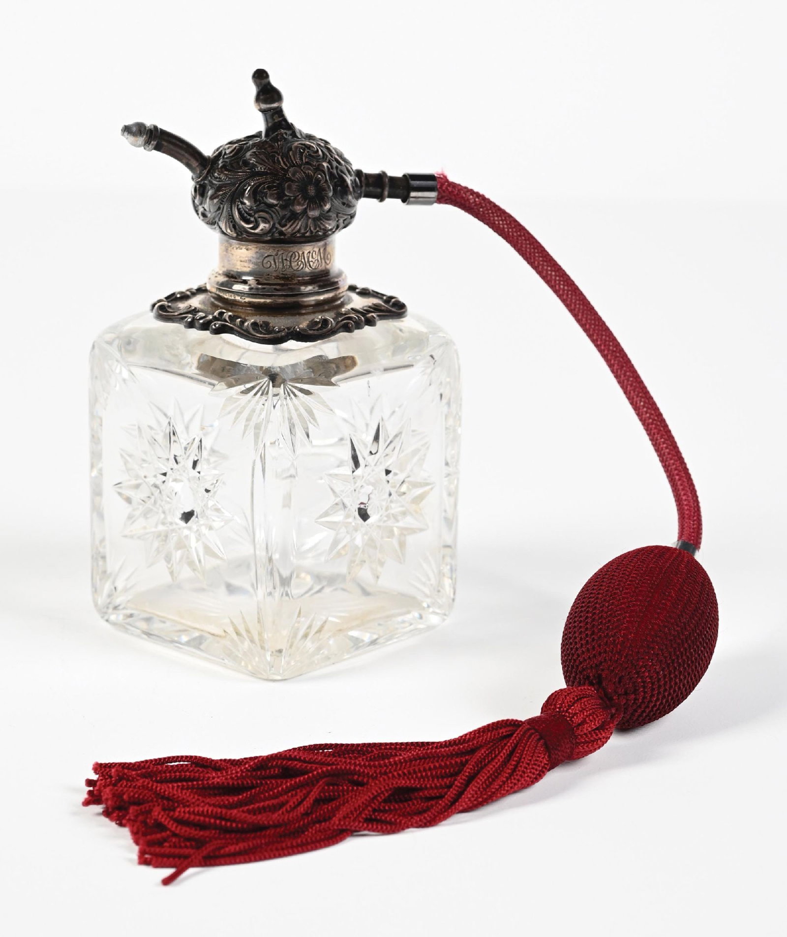 SHORT CUT GLASS PERFUME WITH STERLING TOPPER WITH FLORAL PATTERN AND MAROON ATOMIZER: C. 1990s. A fantastic signed sterling silver and cut-glass perfume atomizer with a maroon cloth puff atomizer. The bottle features a square-shaped, clear-cut glass body with a prominent starburst patt