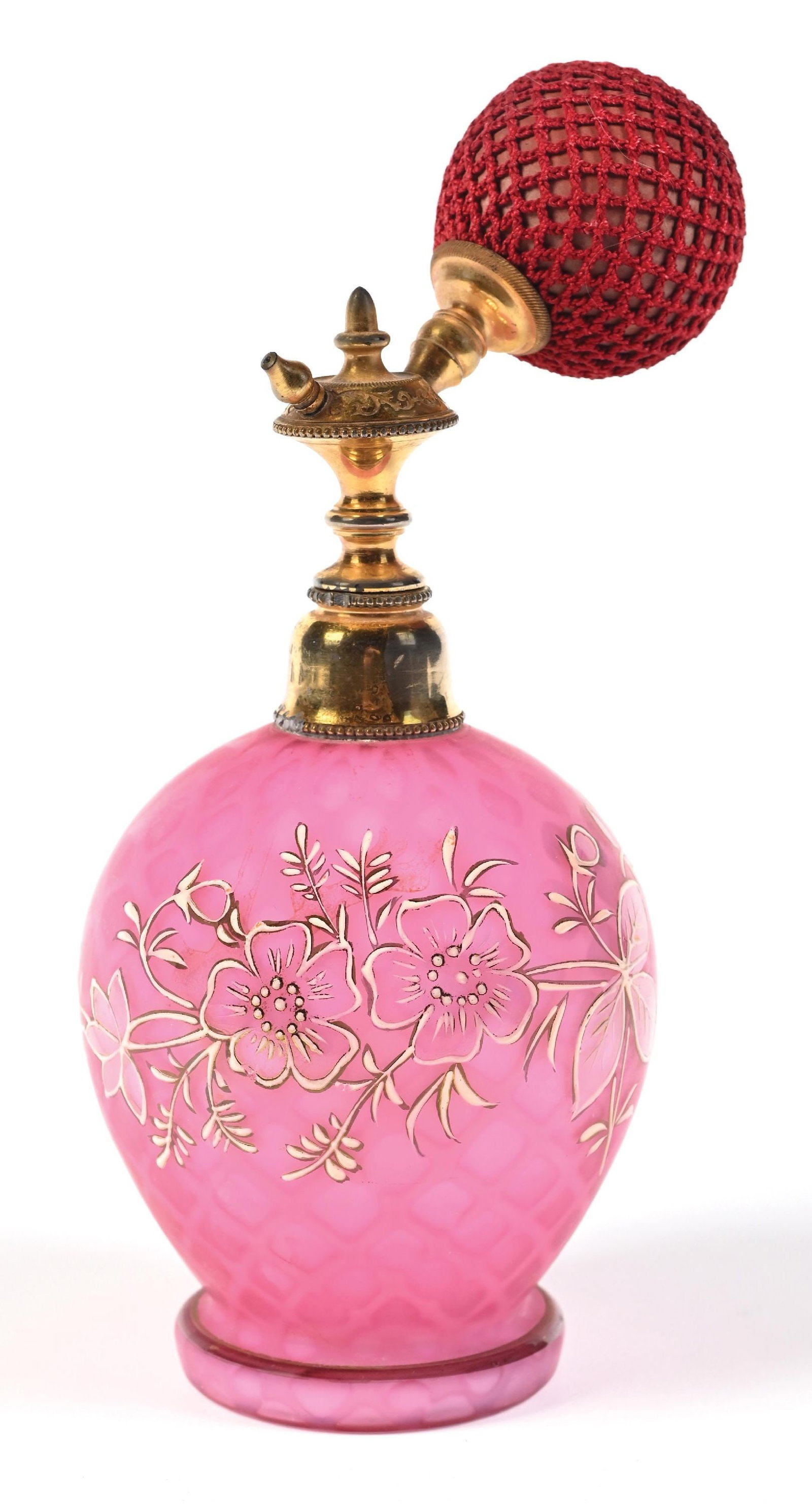 PINK OPALESCENT GLASS PERFUME ATOMIZER: C. 1900s. A rounded pink glass bottle featuring an intricate floral pattern. The glass has a satin finish with a background pattern reminiscent of a fish net. The top is fitted with gold-toned hardwar