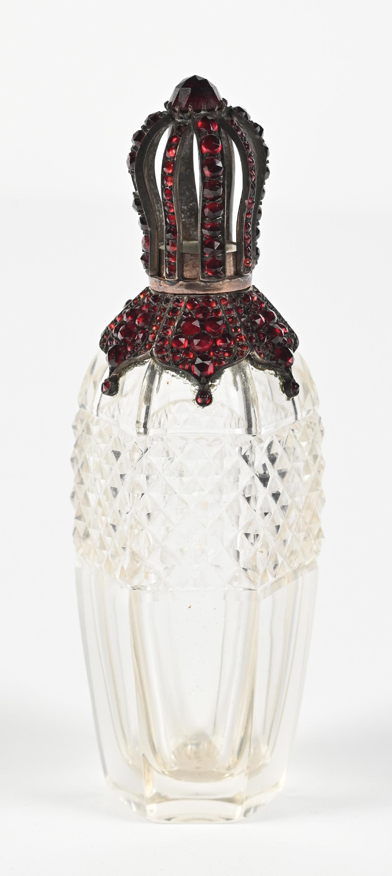 MINIATURE JEWELED GARNET CROWN PERFUME BOTTLE: C. 1900s. A vintage cut-glass perfume bottle featuring a pineapple cut pattern, the collar is adorned with a silver-toned metal top with intricately set deep red rhinestones in an elongated crown-like