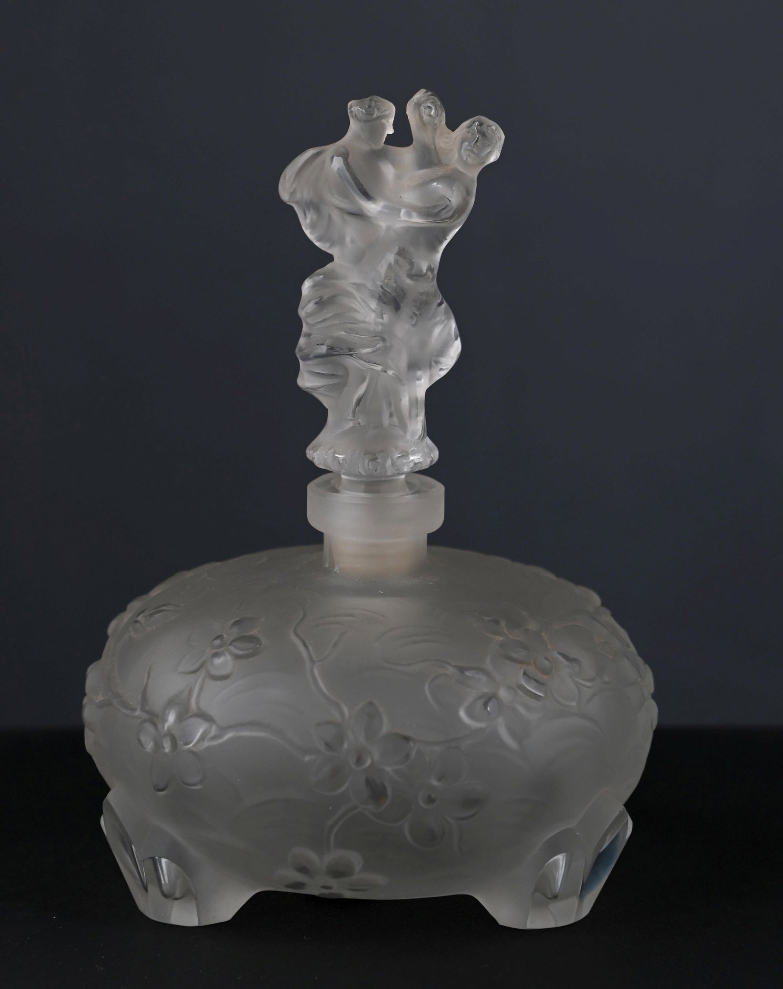 INGRID ART DECO FROSTED GLASS PERFUME BOTTLE: c. 1920S. Ingrid Art Deco frosted glass perfume bottle, decorated with a floral motif around the body and raised on three feet. The original Ingrid paper label remains affixed to the base. The figural