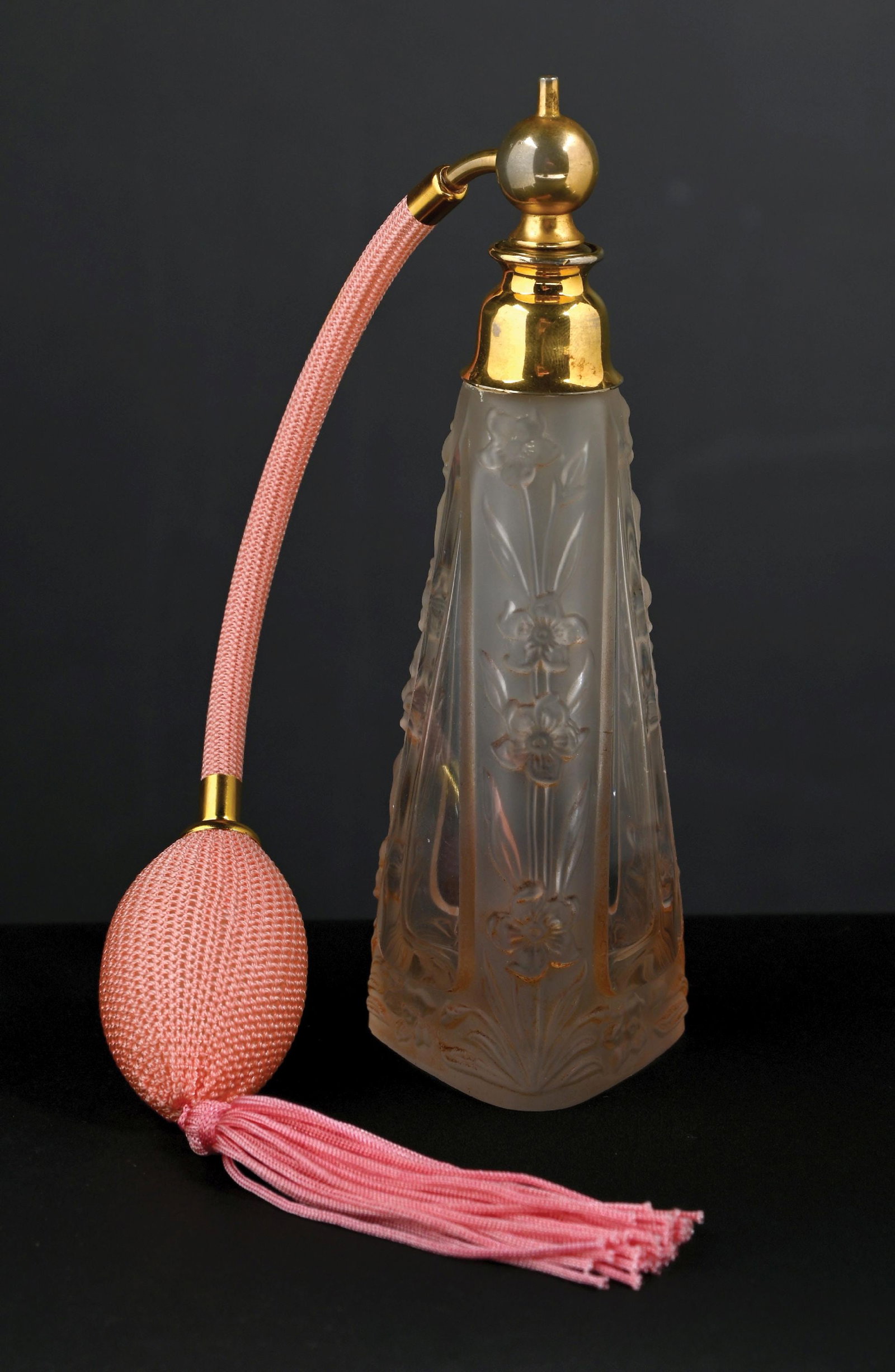 PINK GLASS FLORAL PERFUME WITH ATOMIZER: C. 1920s. An attractive, clear-cut glass perfume atomizer featuring a floral intaglio design with a tapered, faceted shape. The perfume has gold-toned hardware. The perfume has a pink hose and a funct