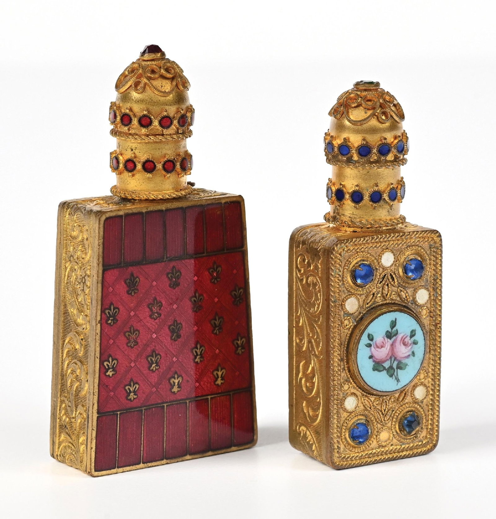 LOT OF 2: ORNATE CZECH PERFUME BOTTLES WITH GOLD-TONE METALWORK: C. 1800s. A collection of two Czech gold-toned metal perfumes with extremely ornate sides of the body and a jeweled lid. The larger perfume has a red enamel plate on the body, while the other has a po