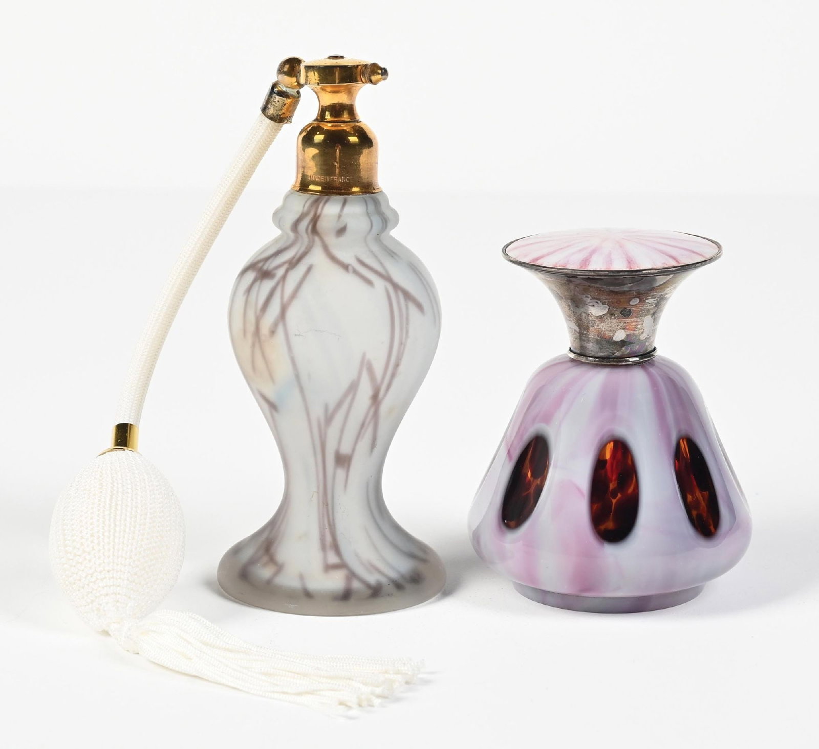 LOT OF 2: PURPLE ART GLASS PERFUME ATOMIZERS: C. 1900s. (A) A unique Loetz-style, frosted, blue, white, and purple-streaked perfume atomizer. It features gold-toned metal fittings with a white tasseled functional squeeze puff. In great condition.