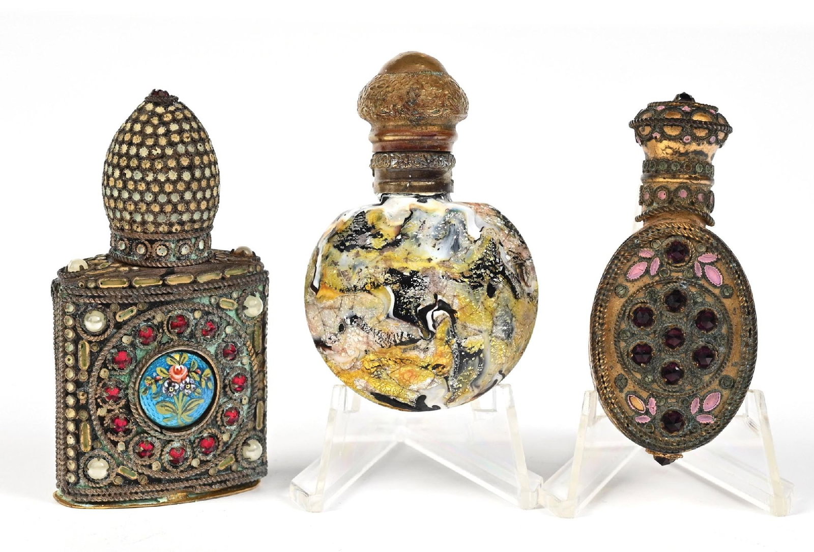 LOT OF 3: METAL-CLAD & JEWELED PERFUME BOTTLES: C. 1800s. A collection of decorative, ornate perfumes featuring jeweled Czech filigree, ornate metal cladding, rhinestone jeweling, and Venetian glass. One stopper is stuck inside the bottle, while an