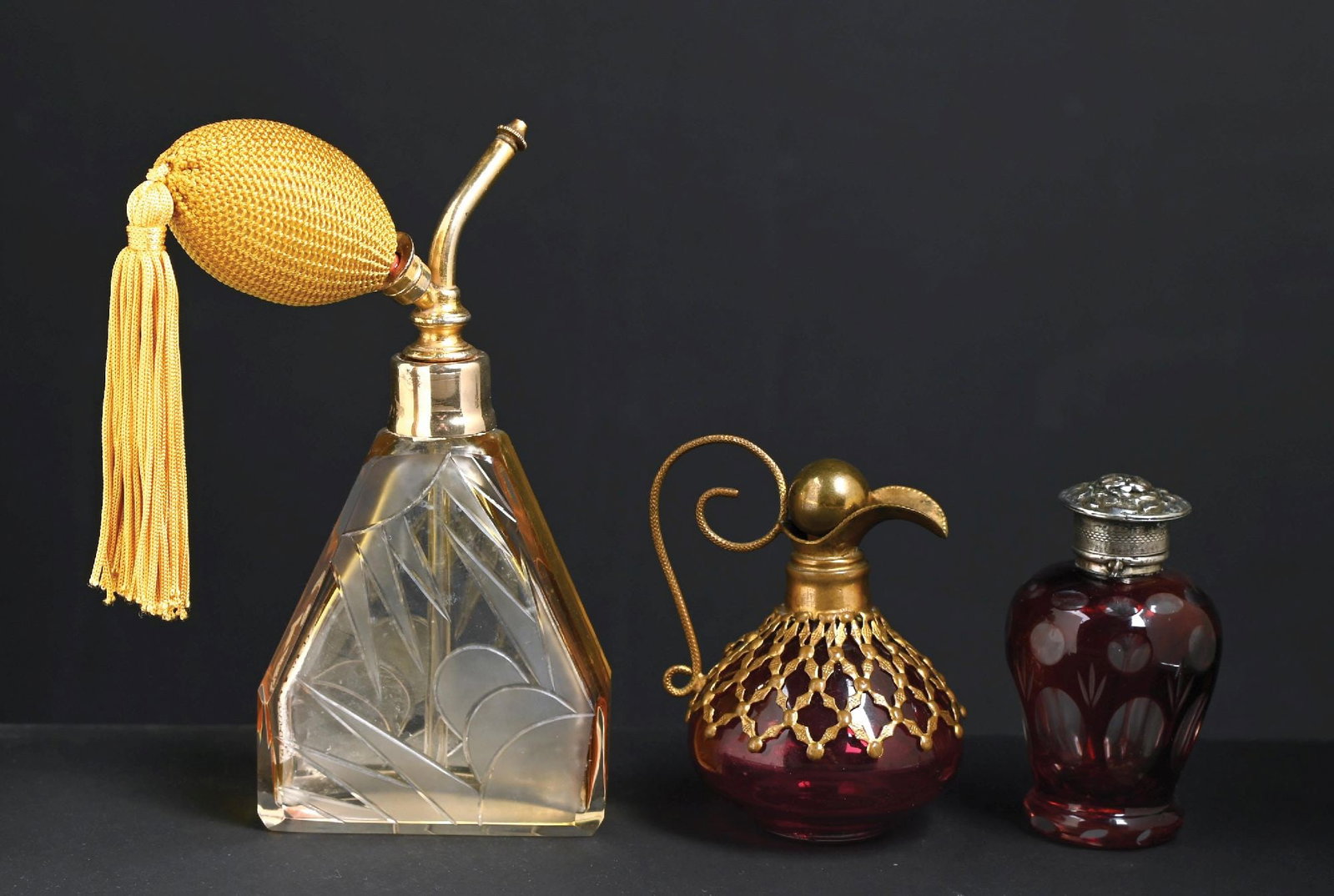 LOT OF 3: CUT GLASS PERFUME BOTTLES & ATOMIZER: C. 1900s. (A) A charming etched yellow and clear glass perfume with designs on the body reminiscent of a sun and clouds. The perfume has a yellow functional tasseled atomizer puff. In great condition.