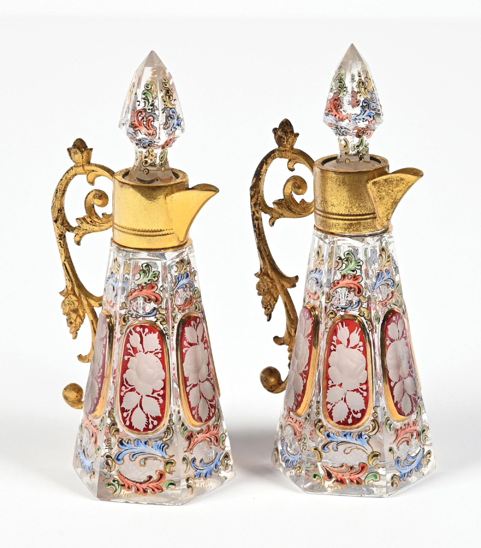LOT OF 2: MOSER BOHEMIAN GLASS JUG PERFUME BOTTLES: C. 1900s. A spectacular pair of Moser Bohemia enameled glass cruets. The body is made of clear faceted glass, featuring a tapered hexagonal shape, and is elaborately decorated with enameled and engrav