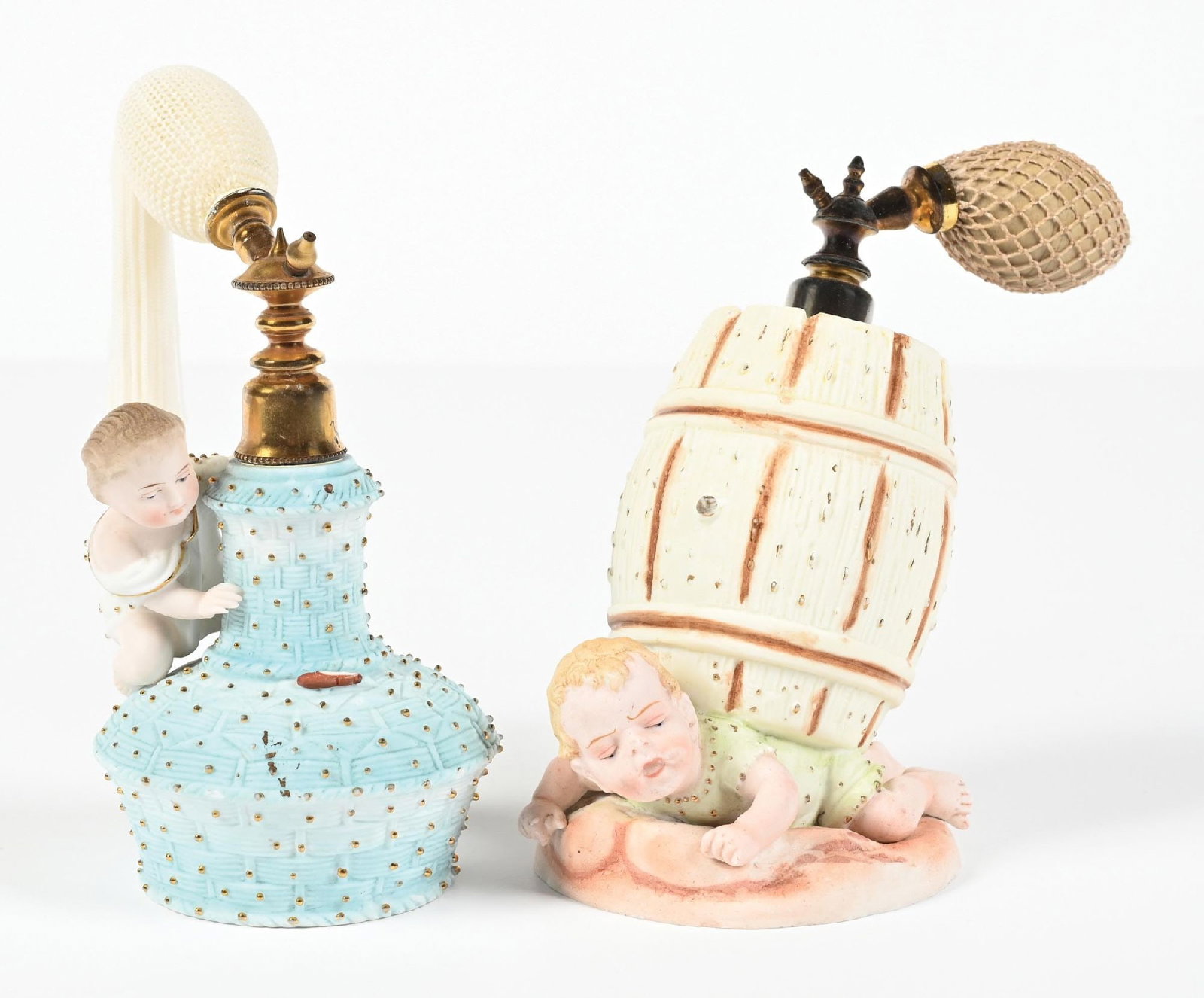 LOT OF 2: PORCELAIN FIGURAL PERFUME ATOMIZERS: C. 1900s. (A) A unique bisque figural perfume atomizer. The perfume features a baby beneath a barrel, with the metal perfume hardware. The gold-tone metal hardware has typical age, and the light pink