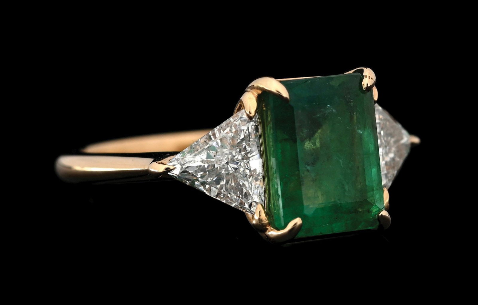 18K YELLOW GOLD EMERALD & DIAMOND RING: 18k yellow gold emerald and diamond ring consisting of 1 emerald cut emerald weighing 1.85cts and 2 trillion cut natural diamonds with a total weight of 1.00cts. Width at top measures 9.5mm. Finger si
