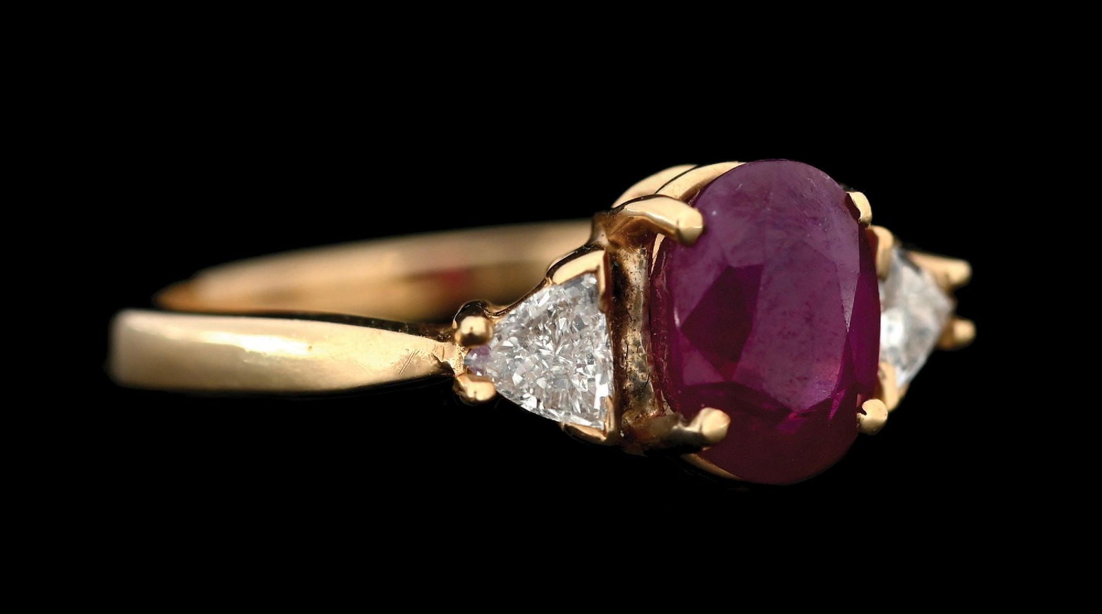 14K YELLOW GOLD RUBY & DIAMOND RING: 14k yellow gold ruby and diamond ring consisting of 1 oval cut ruby weighing 2.05cts and 2 trillion cut natural diamonds with a total weight of 0.40cts. Width at top measures 8mm. Finger size 7. Gross