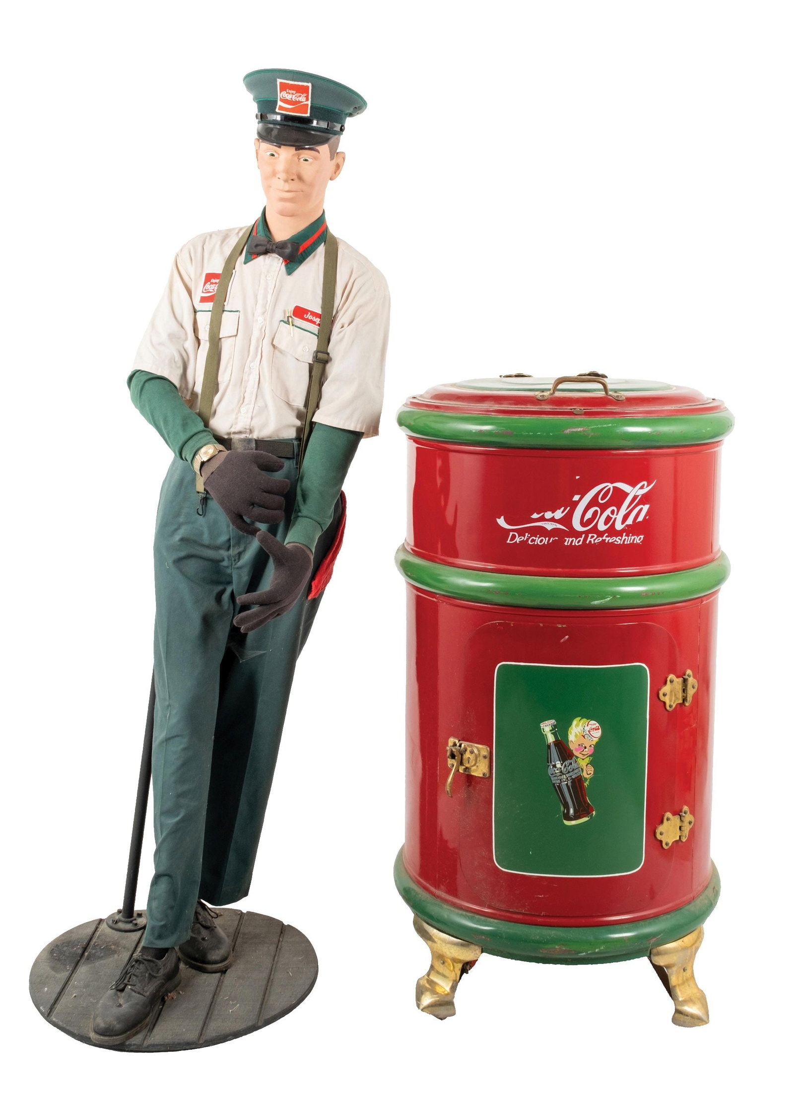 EARLY CYLINDRICAL ICEBOX RESTORED IN COCA-COLA MOTIF W/ COCA-COLA UNIFORMED MANNEQUIN: CONDITION: Refrigerator shows an older restoration with new paint and oxidized brass hinges and handle, showing some light denting overall due to handling, and some areas of lifting paint. The mannequ