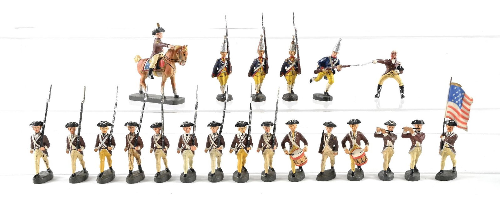 LOT OF 21: PRE-WAR ELASTOLIN REVOLUTIONARY WAR COLONIALS & HESSIANS: Includes: Colonials Marching Shoulder Arms with Officer; Drummers; Pipers; 2 George Washington Mounted figures, 1 without horse; and 4 Hessians, 3 Marching and 1 Advancing, with play wear. Condition: 