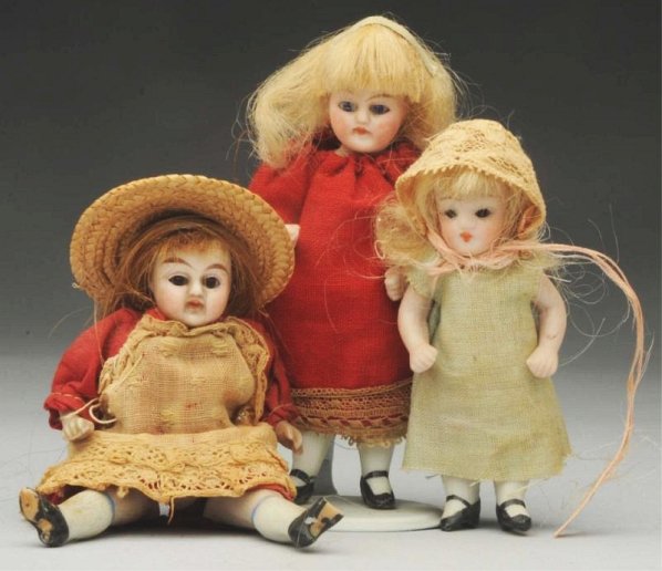 Lot of 3: German All-Bisque Dolls.: Slender girl with glass eyes, scrappy wig, original dress (hole in apron) and straw hat (toe off); slender girl with glass eyes, original wig, replaced red dress; tiny girl with sweet face, glass eyes