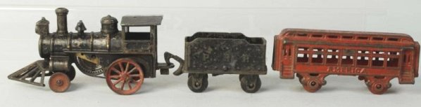 Cast Iron Clockwork Train Set.: American made. American style engine with cow catcher, clockwork mechanism underneath. Working. P.R.R. separate embossed tender and one passenger car marked American on both sides. Condition (Very Goo