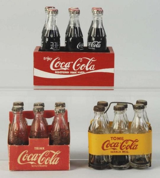 Lot of 3: Small Coca-Cola 6-Pack Carriers.: German cardboard, Spanish metal carrier with wire handle, and Middle Eastern bottles in wooden case. Only light to very moderate wear. Condition (Excellent - Near Mint). Size Largest: 3 - 1/2" L.