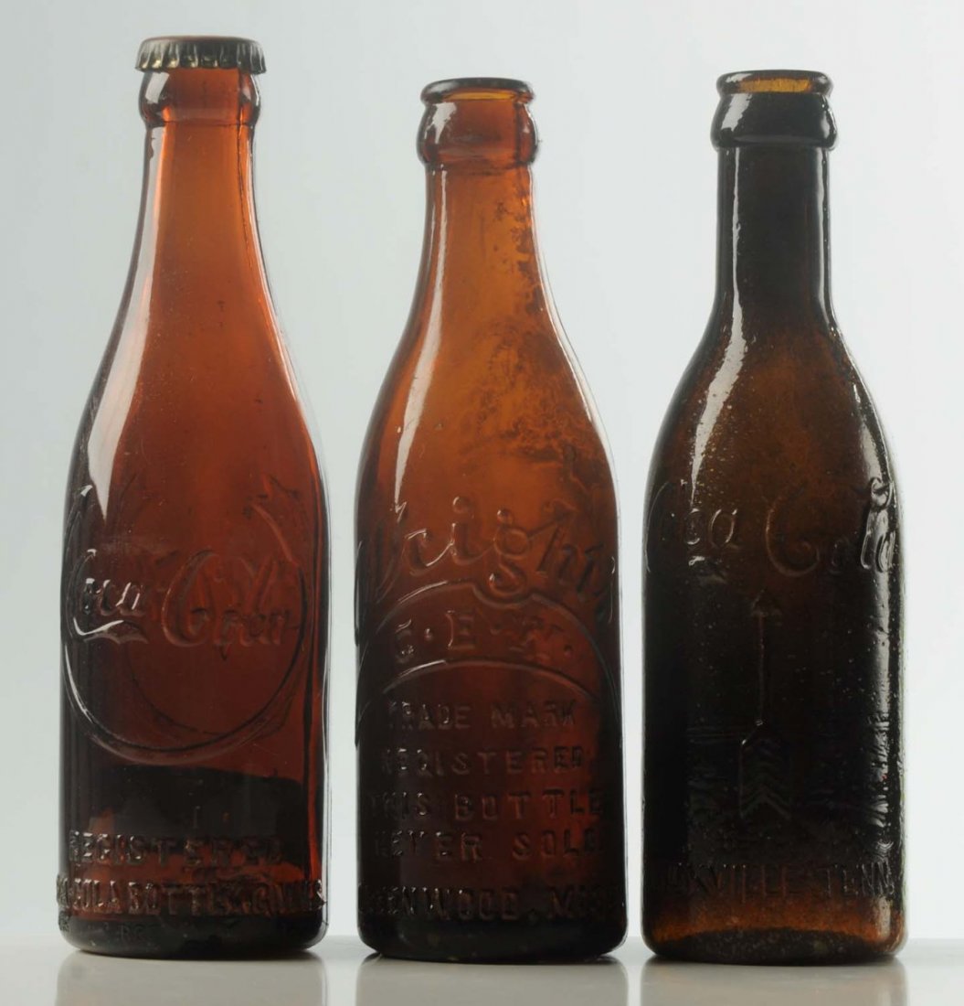 Lot of 3: Glass Coca-Cola Bottles.: Amber in color. Includes examples from Jackson, Tennessee. Knoxville, Tennessee. Greenwood, Mississippi. Small chip on the base of the Jackson, Tennessee example. Condition (Excellent). Size Largest: