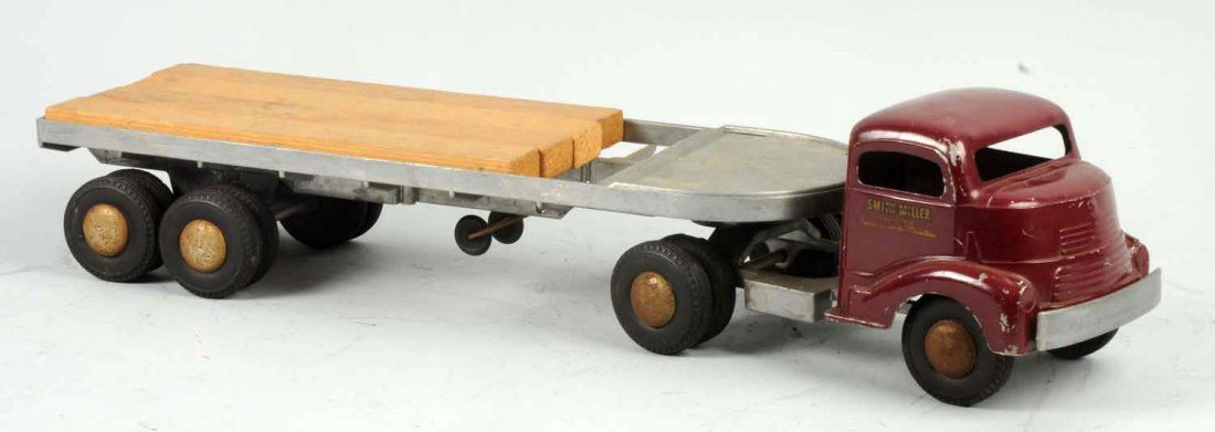 Pressed Steel Smith-Miller Tractor Trailer Truck.: Maroon front Smith- Miller decals on sides. Lumber slats on back. Oxidation to bare metal parts. Chipping and wear to cab. Condition (Very Good). Size 23" L.