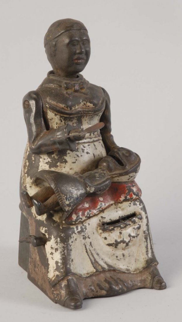 Mammy with Spoon Mechanical Bank.: Manufactured by Kyser and Rex. It is in working condition and comes in a light brown dress variation. The bank depicts mother feeding a baby on her lap. There are significant paint chips and scratches