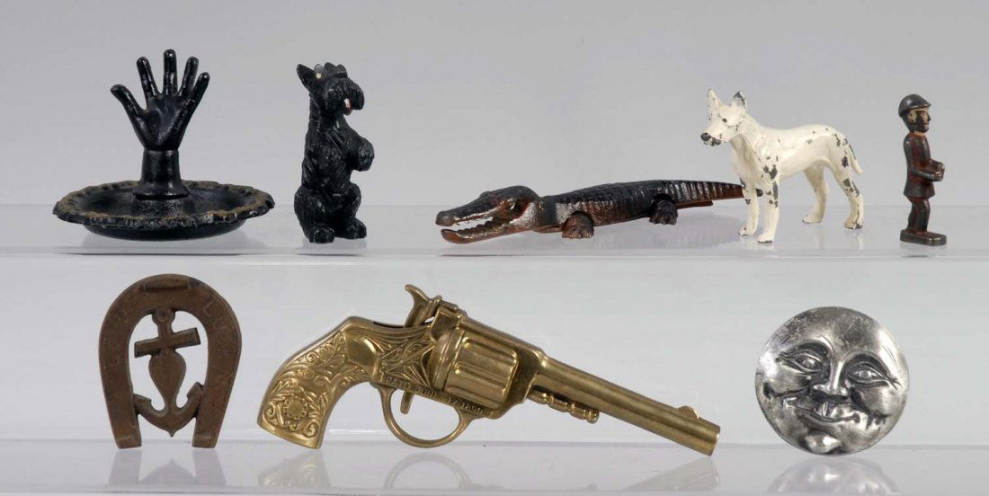 Lot of 8: Assorted Cast Iron Figural Grouping.: Includes moon face belt buckle, ring holder, alligator nut cracker, horseshoe paperweight, brass cap pistol, and white metal Scottie broken tail, etc. Condition (Good). Size Largest: 6 - 7/8" T.