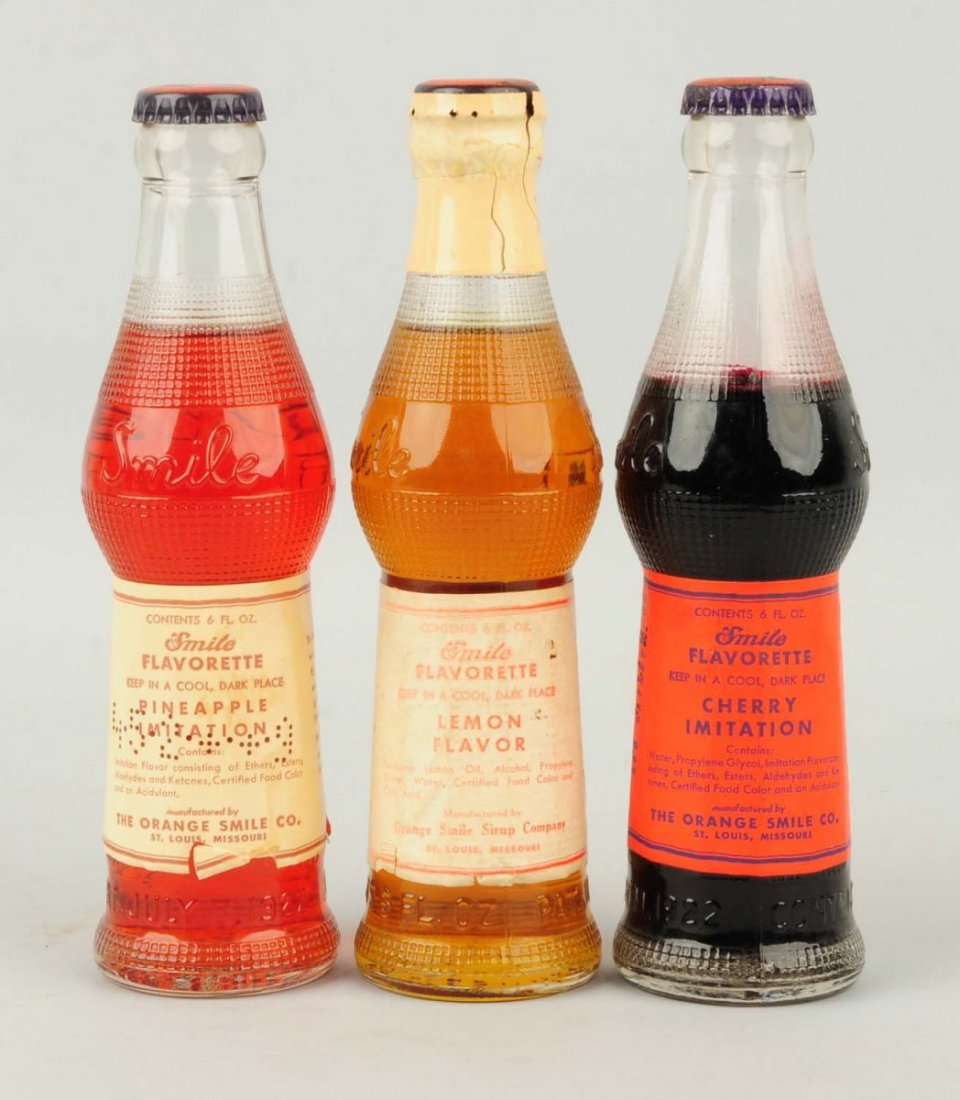 Lot of 3: 1920s Smile Flavorette Bottles.: Each makes one gallon of syrup when sugars and water is added. All are unopened and have graphic Smile bottle caps. Condition (Excellent). Size Each: 7 - 3/4" T.