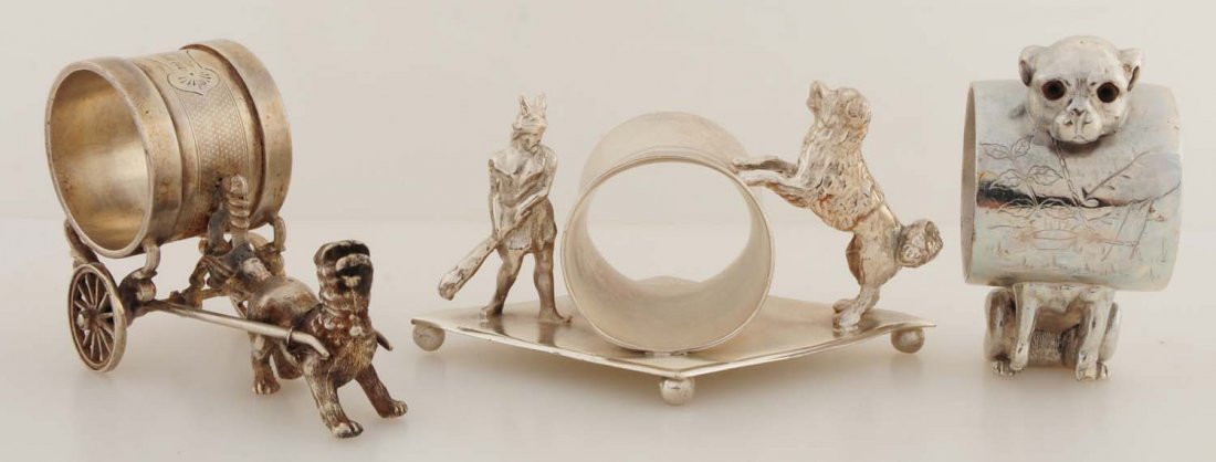 Lot of 3: Figural Napkin Rings.: First napkin ring has a small Viking-type figure with a club on one side of the napkin holder, and a large fluffy dog with its front paws on the napkin holder on the other side. On a diamond-shaped, b