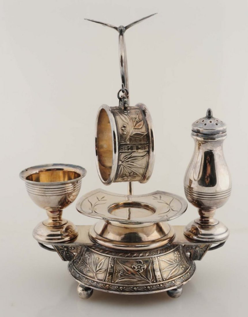 Figural Napkin Ring Combination Set.: A ball-footed, raised, round base is beautifully decorated with flowers, leaves, and other Victorian designs. Resting atop the base is a pepper shaker, butter plate, and open salt. A tall handle goes 